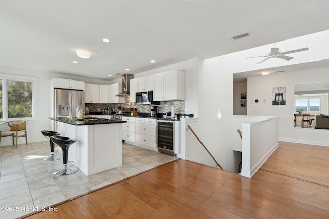 kitchen featuring white cabinetry, wall chimney range hood, wine cooler, light hardwood / wood-style flooring, and a kitchen bar