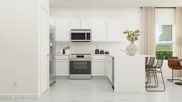 kitchen with kitchen peninsula, stainless steel refrigerator with ice dispenser, a kitchen breakfast bar, electric range oven, and white cabinets