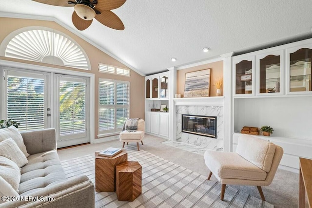 carpeted living room with a textured ceiling, vaulted ceiling, ceiling fan, crown molding, and a premium fireplace