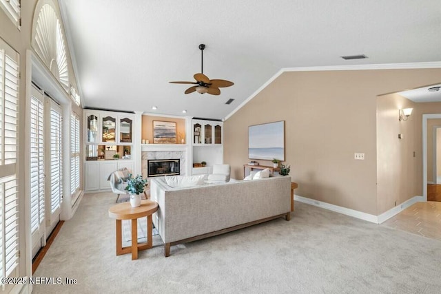 living room featuring vaulted ceiling, built in shelves, ceiling fan, ornamental molding, and light colored carpet