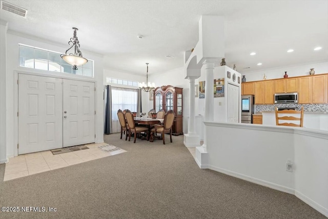 foyer with a notable chandelier, ornate columns, and light carpet