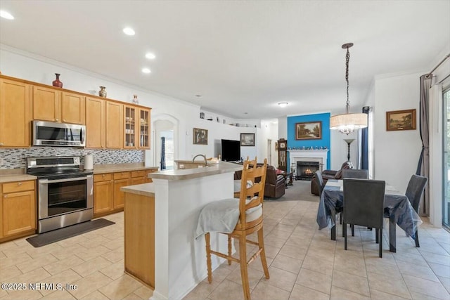 kitchen featuring decorative backsplash, appliances with stainless steel finishes, crown molding, decorative light fixtures, and a breakfast bar area