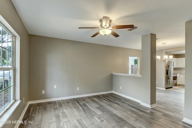 spare room featuring ceiling fan with notable chandelier, light hardwood / wood-style flooring, and plenty of natural light