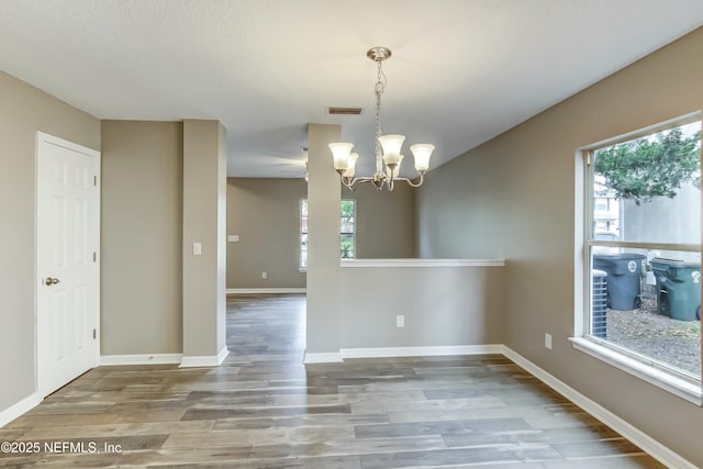 unfurnished dining area featuring plenty of natural light, a chandelier, and hardwood / wood-style flooring