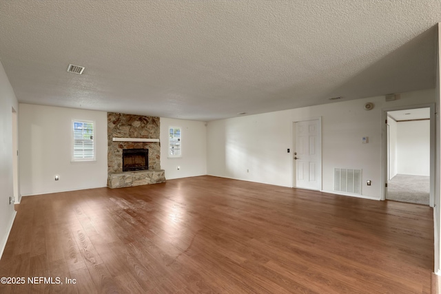 unfurnished living room with a textured ceiling, hardwood / wood-style flooring, and a stone fireplace