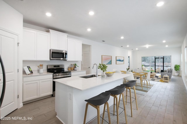 kitchen with a breakfast bar, a kitchen island with sink, sink, white cabinetry, and stainless steel appliances