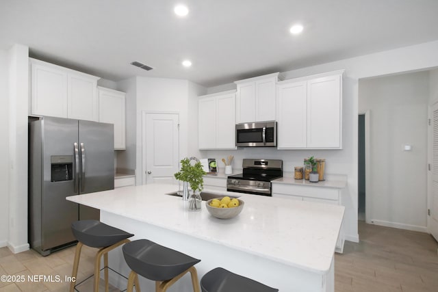 kitchen with white cabinetry, a kitchen island with sink, a breakfast bar area, and appliances with stainless steel finishes