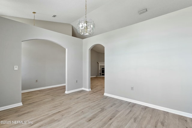 spare room with a chandelier, light hardwood / wood-style flooring, and vaulted ceiling