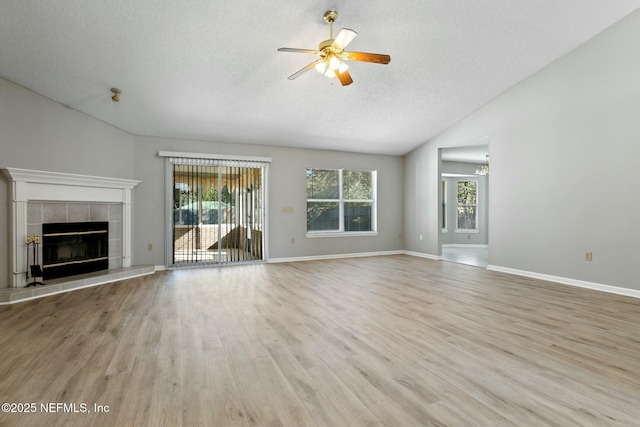 unfurnished living room featuring light hardwood / wood-style flooring, a textured ceiling, lofted ceiling, a fireplace, and ceiling fan with notable chandelier