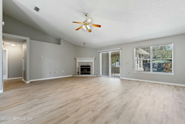 unfurnished living room with ceiling fan, light hardwood / wood-style floors, lofted ceiling, and a tiled fireplace