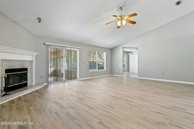 unfurnished living room with a tile fireplace, ceiling fan, light hardwood / wood-style floors, a textured ceiling, and vaulted ceiling