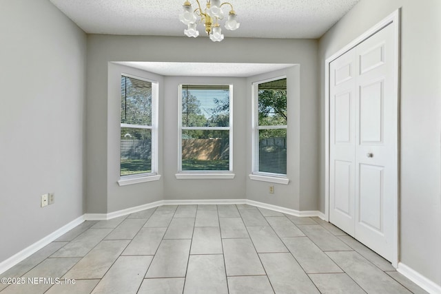 unfurnished dining area with light tile patterned floors, a textured ceiling, and a notable chandelier