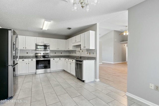 kitchen with dark stone counters, stainless steel appliances, vaulted ceiling, sink, and white cabinets