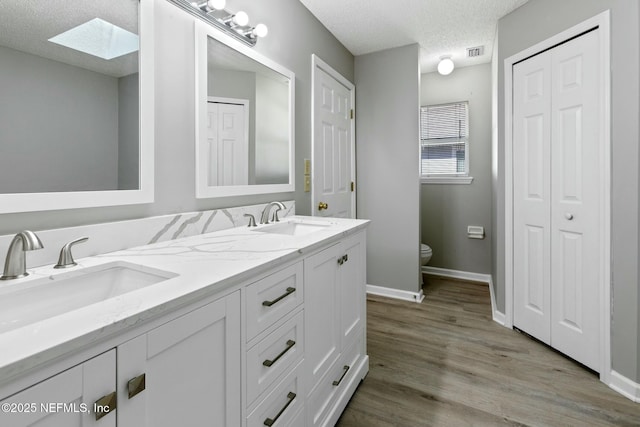 bathroom with a skylight, vanity, a textured ceiling, hardwood / wood-style flooring, and toilet