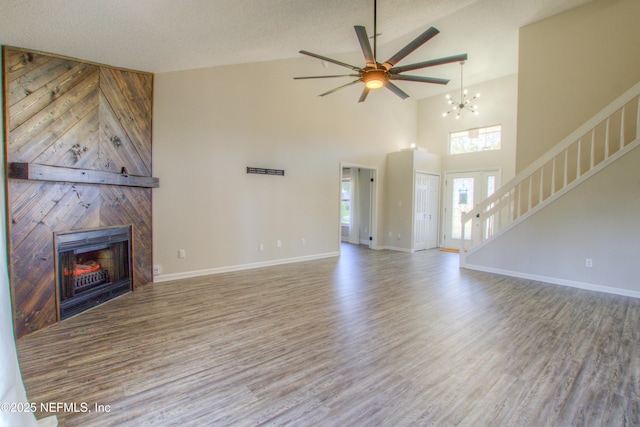 unfurnished living room featuring a large fireplace, high vaulted ceiling, hardwood / wood-style floors, a textured ceiling, and ceiling fan with notable chandelier