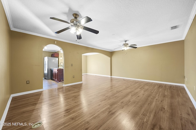 empty room with a textured ceiling, wood-type flooring, sink, ornamental molding, and ceiling fan