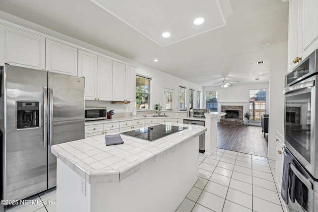 kitchen with white cabinets, stainless steel appliances, light tile patterned floors, a fireplace, and a center island