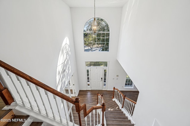 foyer entrance with hardwood / wood-style flooring, a towering ceiling, a wealth of natural light, and an inviting chandelier