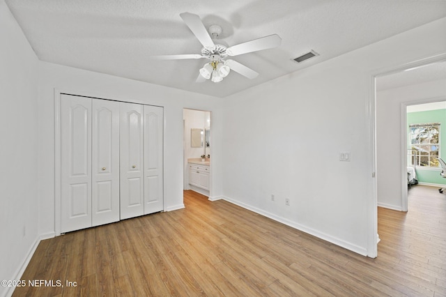 unfurnished bedroom featuring ensuite bathroom, a textured ceiling, ceiling fan, light hardwood / wood-style flooring, and a closet