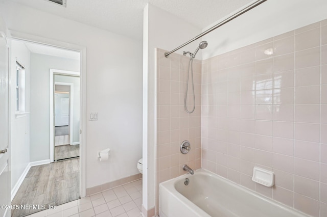 bathroom with tile patterned floors, tiled shower / bath combo, a textured ceiling, and toilet