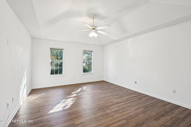 empty room featuring a raised ceiling, ceiling fan, dark wood-type flooring, and a textured ceiling