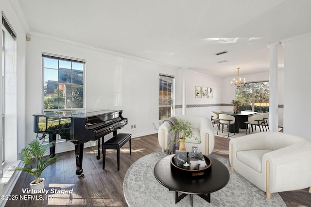 living area featuring dark hardwood / wood-style flooring, ornate columns, crown molding, and an inviting chandelier