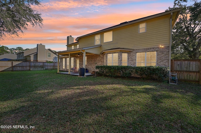 back house at dusk featuring ceiling fan, a patio area, and a yard