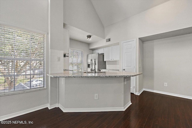 kitchen featuring kitchen peninsula, stainless steel refrigerator with ice dispenser, light stone counters, vaulted ceiling, and white cabinetry