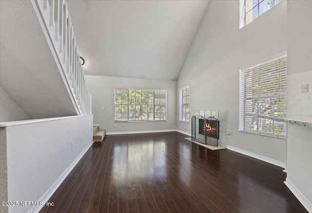 unfurnished living room with a tiled fireplace, high vaulted ceiling, and dark wood-type flooring