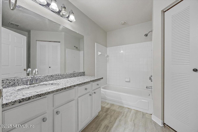 bathroom featuring a textured ceiling, vanity, tiled shower / bath, and hardwood / wood-style floors