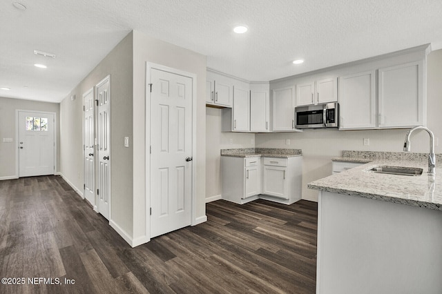 kitchen featuring light stone countertops, dark hardwood / wood-style flooring, a textured ceiling, sink, and white cabinets