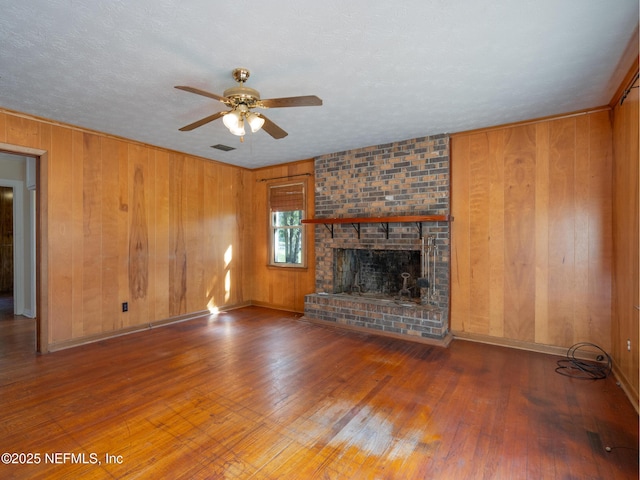 unfurnished living room featuring a brick fireplace, a textured ceiling, ceiling fan, wooden walls, and wood-type flooring