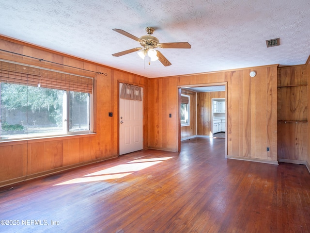 unfurnished room featuring ceiling fan, dark hardwood / wood-style floors, a textured ceiling, and wooden walls