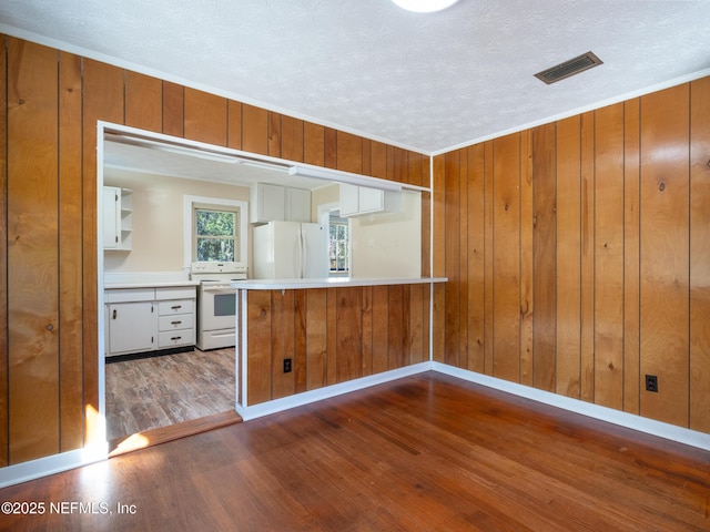 kitchen featuring a textured ceiling, white appliances, white cabinetry, and wood walls