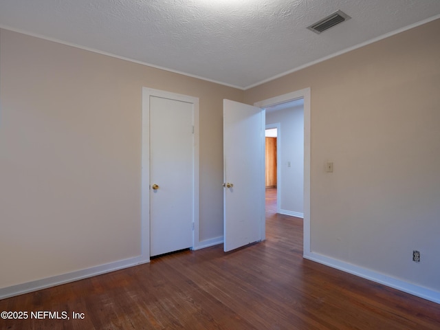 spare room with a textured ceiling, crown molding, and dark wood-type flooring