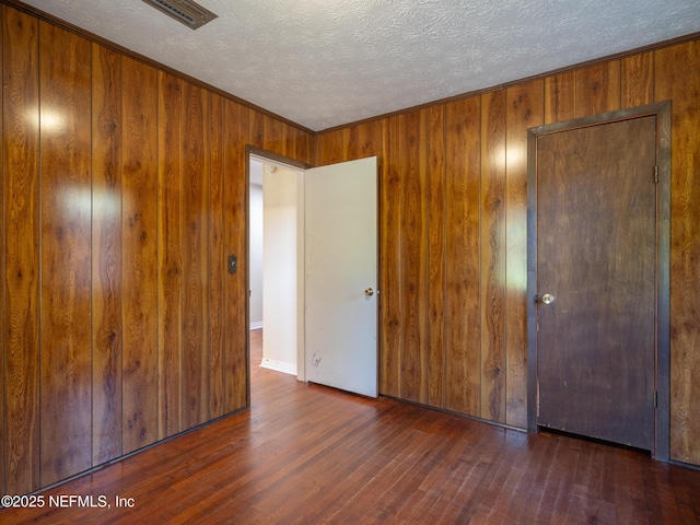 unfurnished bedroom featuring a textured ceiling, dark wood-type flooring, wooden walls, and a closet