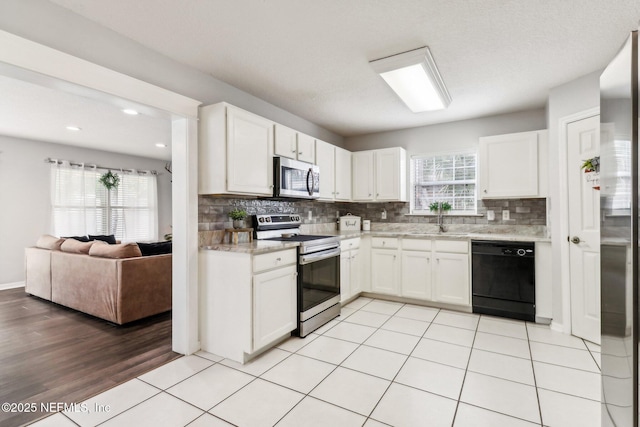 kitchen with stainless steel appliances, white cabinetry, a healthy amount of sunlight, and light tile patterned flooring