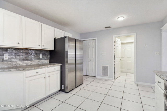 kitchen with white cabinets, decorative backsplash, light tile patterned floors, and stainless steel refrigerator