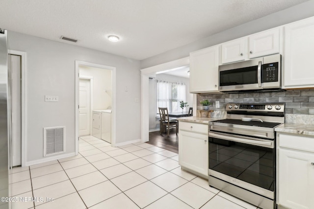 kitchen featuring white cabinets, decorative backsplash, washing machine and dryer, light tile patterned floors, and stainless steel appliances