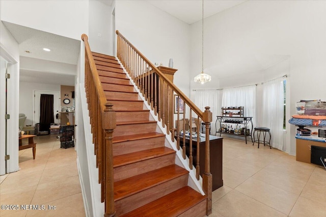 stairway featuring tile patterned floors, an inviting chandelier, and a high ceiling