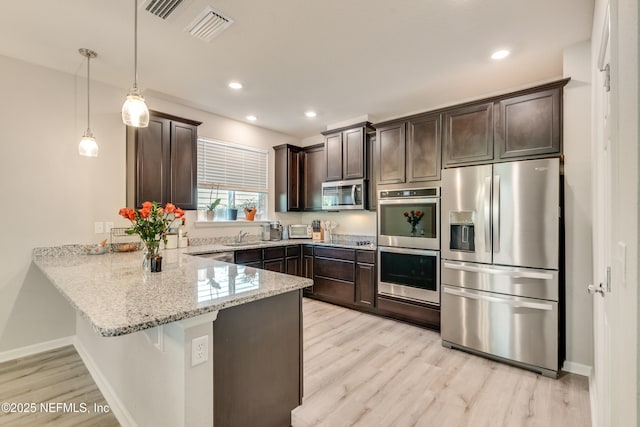 kitchen with kitchen peninsula, appliances with stainless steel finishes, decorative light fixtures, light stone counters, and dark brown cabinetry