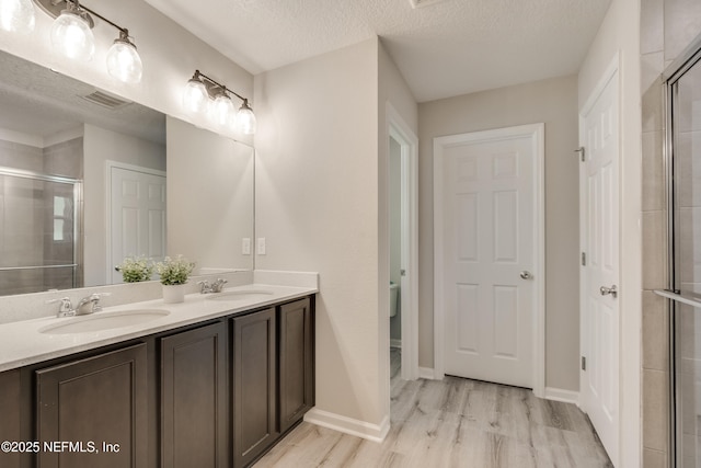 bathroom with vanity, a textured ceiling, a shower with door, hardwood / wood-style flooring, and toilet