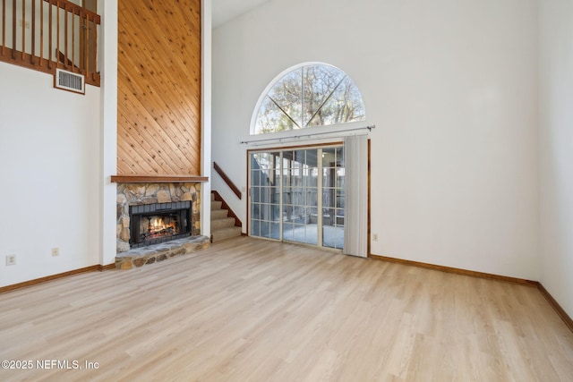 unfurnished living room with a high ceiling, light hardwood / wood-style floors, and a stone fireplace