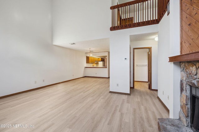 unfurnished living room featuring a stone fireplace, a high ceiling, and light wood-type flooring