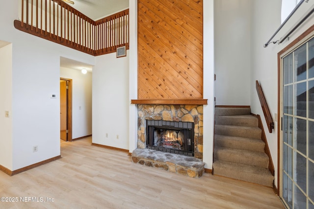 unfurnished living room with a towering ceiling, light hardwood / wood-style flooring, and a stone fireplace