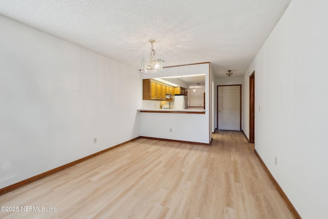 unfurnished living room featuring a textured ceiling, an inviting chandelier, and light hardwood / wood-style flooring