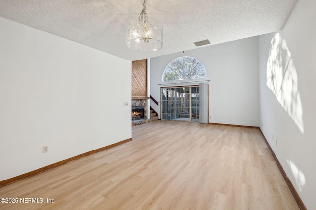 unfurnished living room with a fireplace, light hardwood / wood-style floors, a textured ceiling, and a notable chandelier