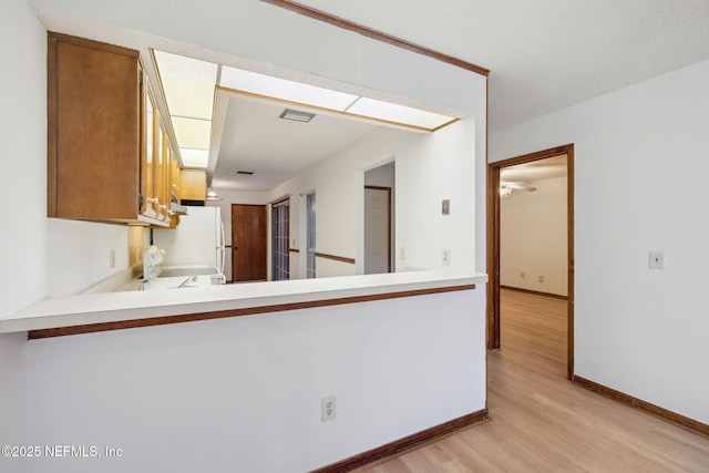 kitchen with ceiling fan, white refrigerator, kitchen peninsula, light wood-type flooring, and range