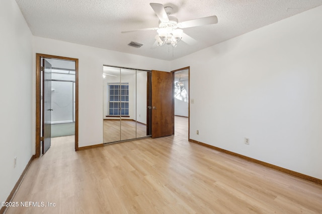 unfurnished bedroom featuring a textured ceiling, a closet, light hardwood / wood-style flooring, and ceiling fan