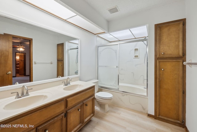 bathroom featuring vanity, bath / shower combo with glass door, hardwood / wood-style flooring, ceiling fan, and a textured ceiling